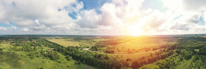 Asphalt road through green summer field and forest near farmland. Aerial panoram