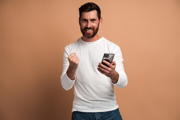 Happy satisfied man with beard holding smartphone and smiling making yes gesture, celebrating...