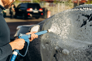 Close up horizontal shot of black car with cleaning foam at car wash service outdoors with high...