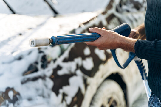 Cropped view of the caucasian young man holding high pressure gun while preparing to spraying at his car during the cleaning. Stock photo
