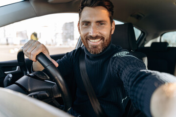 Great selfie. Handsome bearded man holding camera and making selfie while sitting in the car at the...