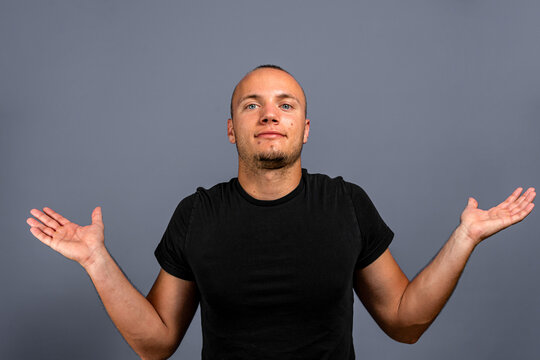 I don't know. Portrait of confused handsome young man in blue casual style black shirt looking at camera with answer. indoor studio shot, isolated on gray background.