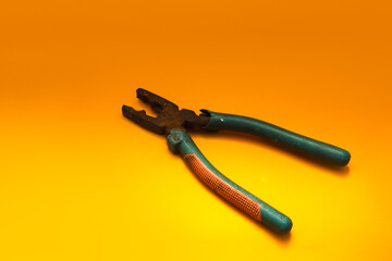 Old used rusty pliers with green grip isolated on orange background.