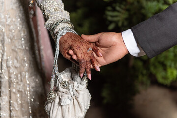 Medndi henna tattoo covers the hands of the bride in as groom holds her hand in his on wedding day