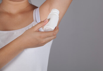 Woman applying deodorant, gray background.
