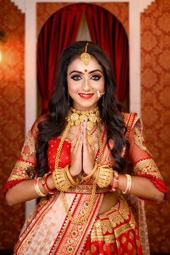 Portrait of very beautiful young Indian lady in luxurious costume with makeup and heavy jewellery, standing with her hands in a namaste gesture