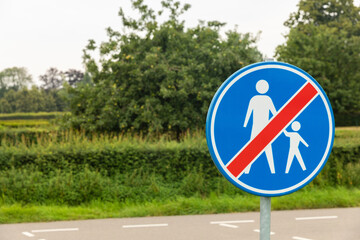 Traffic sign meaning the end of the pedestrian zone, shown by a grown up person and a child walking icon on a blue background, crossed by with a red line.