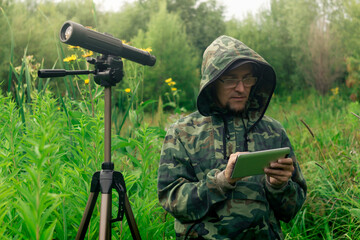ornitologist looks at or writes down information on the tablet while standing among the tall grass...