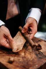 closeup of hands of a man rolling a cigar and tobacco leaf