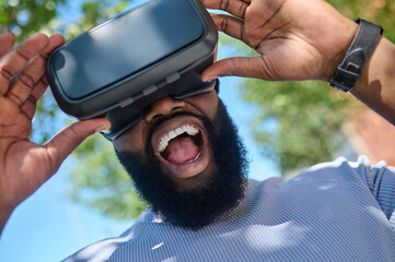 A dark-skinned man in a white tshirt in vr glasses looking excited