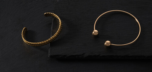 Fototapeta na wymiar Top view of Two modern gold braid shape bracelets on black stone trays