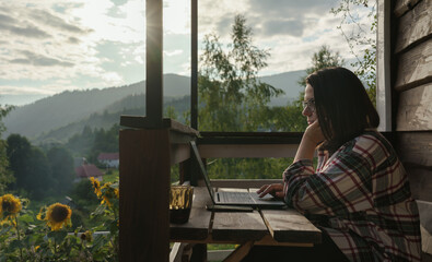 Woman working on computer outdoor on terrace with mountain view