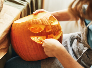 Cropped shot of woman carving large orange pumpkin while preparing for Halloween party