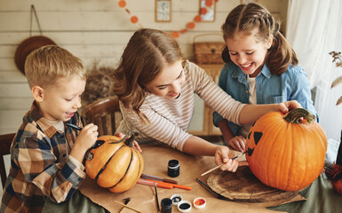 Fototapeta premium Smiling mother with children creating jack-o-lantern during Halloween celebration at home
