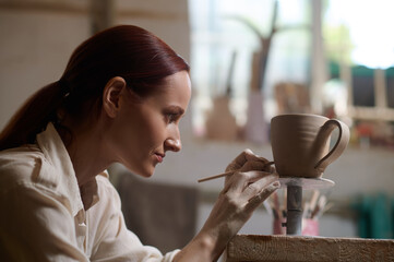 A young woman painting the cup and looking involved