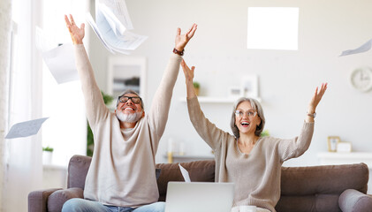 Excited senior family couple throwing up papers documents while paying bills online