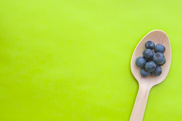 Flat lay of recycled spoon and juicy, fresh blueberries on color table. Space for text. Isolated ripe sweet bilberry fruits in eco spoon on green background. Copy Space. Healthy raw vegetarian food 