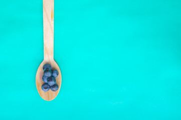 Flat lay of recycled spoon and juicy fresh blueberries on color table. Space for text. Isolated ripe sweet bilberry fruits in eco spoon on turquoise background. Copyspace. Healthy raw vegetarian food 