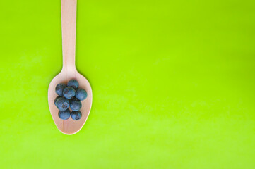 Flat lay of recycled spoon and juicy, fresh blueberries on color table. Space for text. Isolated ripe sweet bilberry fruits in eco spoon on green background. Copy Space. Healthy raw vegetarian food 