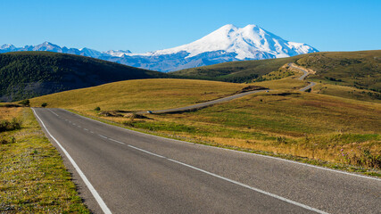 Wavy road through the autumn hills to the distant snowy mountain