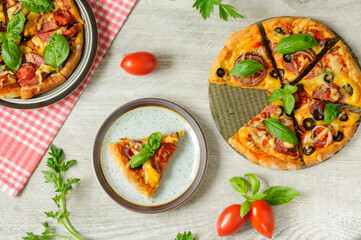 Pizza and slices on a gray background with vegetables and herbs. Top view, flat lay with selective focus and natural lighting