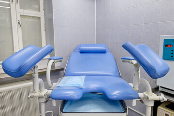 New empty blue gynecological chair in a medical clinic. Front view of the gynecological chair - obrazy, fototapety, plakaty