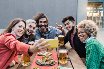 Young multiracial people having fun taking a selfie drinking beer at brewery bar outdoor - Main focus on asian man face