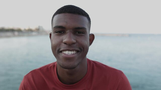 Close up portrait of smiling hispanic man looking at camera by the sea at sunset - Youth, millennial generation and hispanic people concept