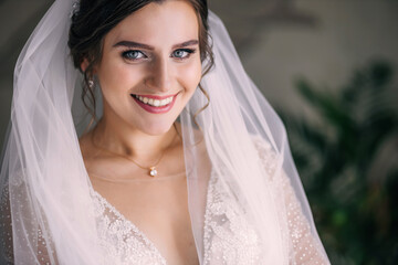 Beautiful bride posing in a wedding dress and veil at home. Beautiful makeup and smiles.