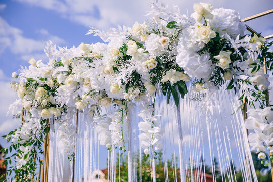 a beautiful arch, a photo zone of newlyweds against the background of the blue sky, decorated with white flowers and green leaves, a ribbon