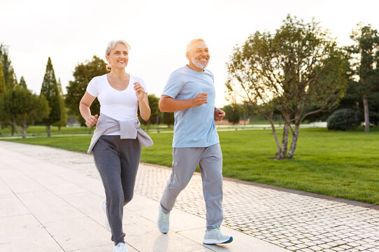 Full-length photo of happy senior husband and wife in sportive outfits running outdoors in city park