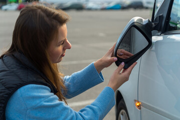 Broken off side rearview mirror on car. Woman is checking for damage on her auto