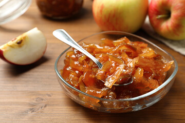 Tasty apple jam in glass bowl and fresh fruit on wooden table, closeup