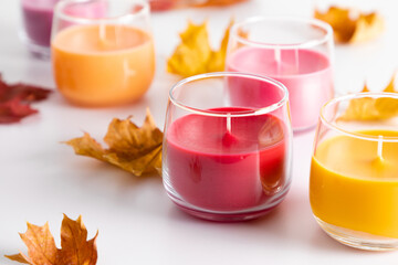 Autumn colorful composition with dry leaves and candles on white background. Beautiful colored candles in glass. Aroma candles with colorful wax.