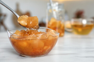 Spoon with delicious apple jam over bowl on white table, closeup