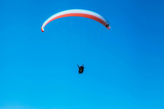 Low angle shot of two people flying a paraplane with clear blue sky in the background