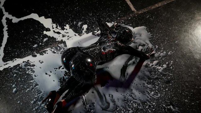 a woman in a black latex suit and high-heeled shoes smears a white liquid on the dark floor with her breasts. top view