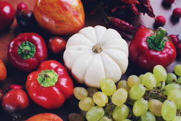 Seasonal composition with pumpkins, grapes, autumn leaves, ripe fruits and vegetables on rustic brown table