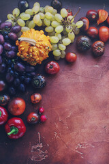 Seasonal composition with pumpkins, grapes, autumn leaves, ripe fruits and vegetables on rustic brown table