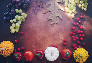 Seasonal composition with pumpkins, grapes, autumn leaves, ripe fruits and vegetables on rustic brown table