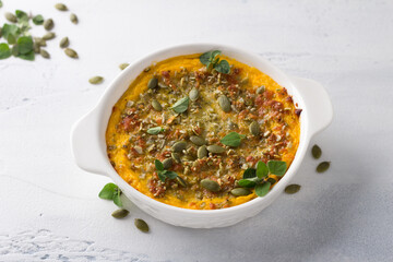 Homemade pumpkin casserole or gratin with cheese and pumpkin seeds in ceramic form on a light gray background
