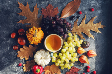 Cozy autumn composition, cup of tea,  pumpkins, grapes, autumn leaves on dark stone table