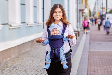 Woman with little boy in baby carrier walks outdoors.