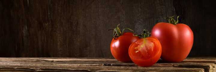 group of ripe fresh tomatoes on old boards against a brown wooden backdrop. panoramic side view. artistic still life in simple rustic style with copy space