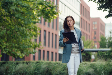Successful beautiful business woman in suit with document walking to the meeting near modern office building.