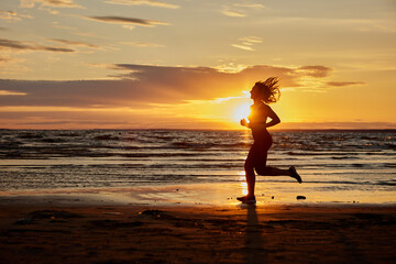 Fototapeta premium Woman runs on shore for being healthy during sunset.