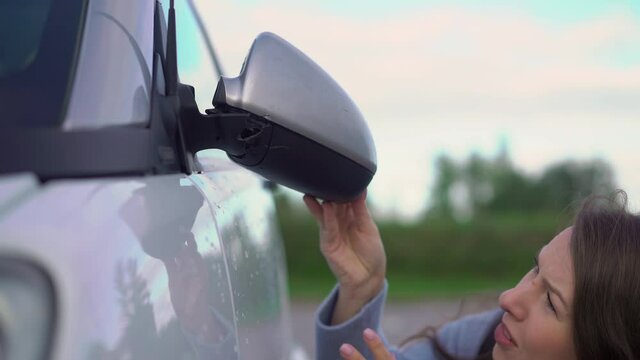 Broken off side rearview mirror on car. Woman is checking for damage on her auto