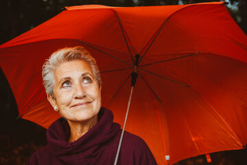 portrait of mature woman with gray hair  holding an orange umbrella on a rainy fall day.