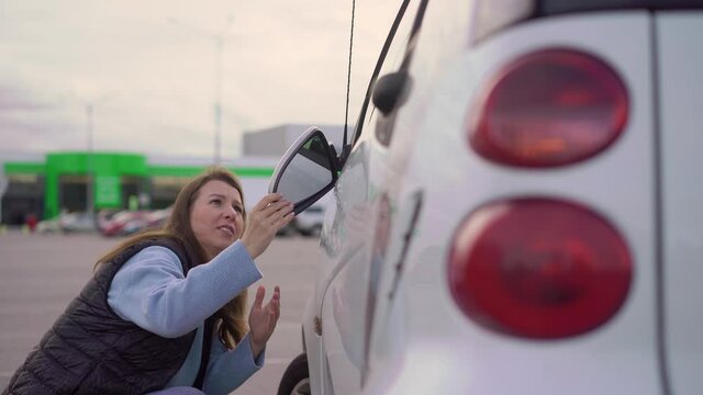 Broken off side rearview mirror on car. Woman is checking for damage on her auto