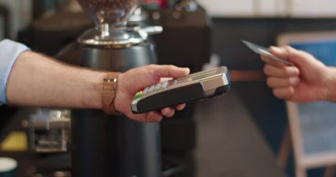 Close up of Caucasian male waiter's hand giving to client coffee-to-go in cafeteria indoors. Man customer taking take away coffee paying for drink with credit card in cafe. Buying, restaurant concept